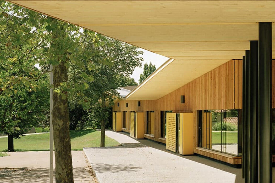 Architecture durable et éco-construction : école en bois-paille. Il y a trois arbres sur la gauche et l'école sur la droite. agence Tectonique Architectes Lyon